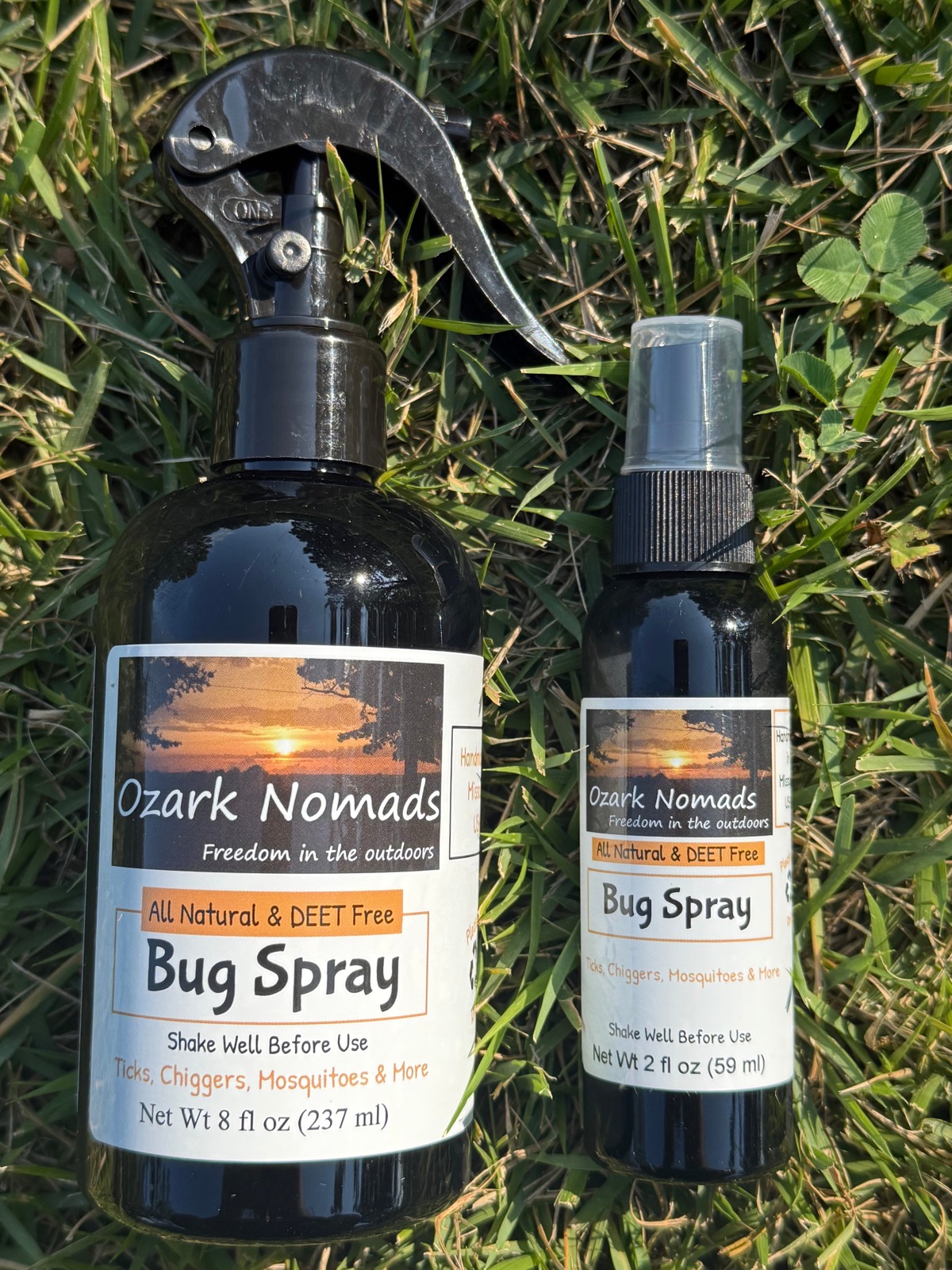 Ozark Nomads All Natural Bug Spray, 8oz and 2oz amber bottles resting on grass